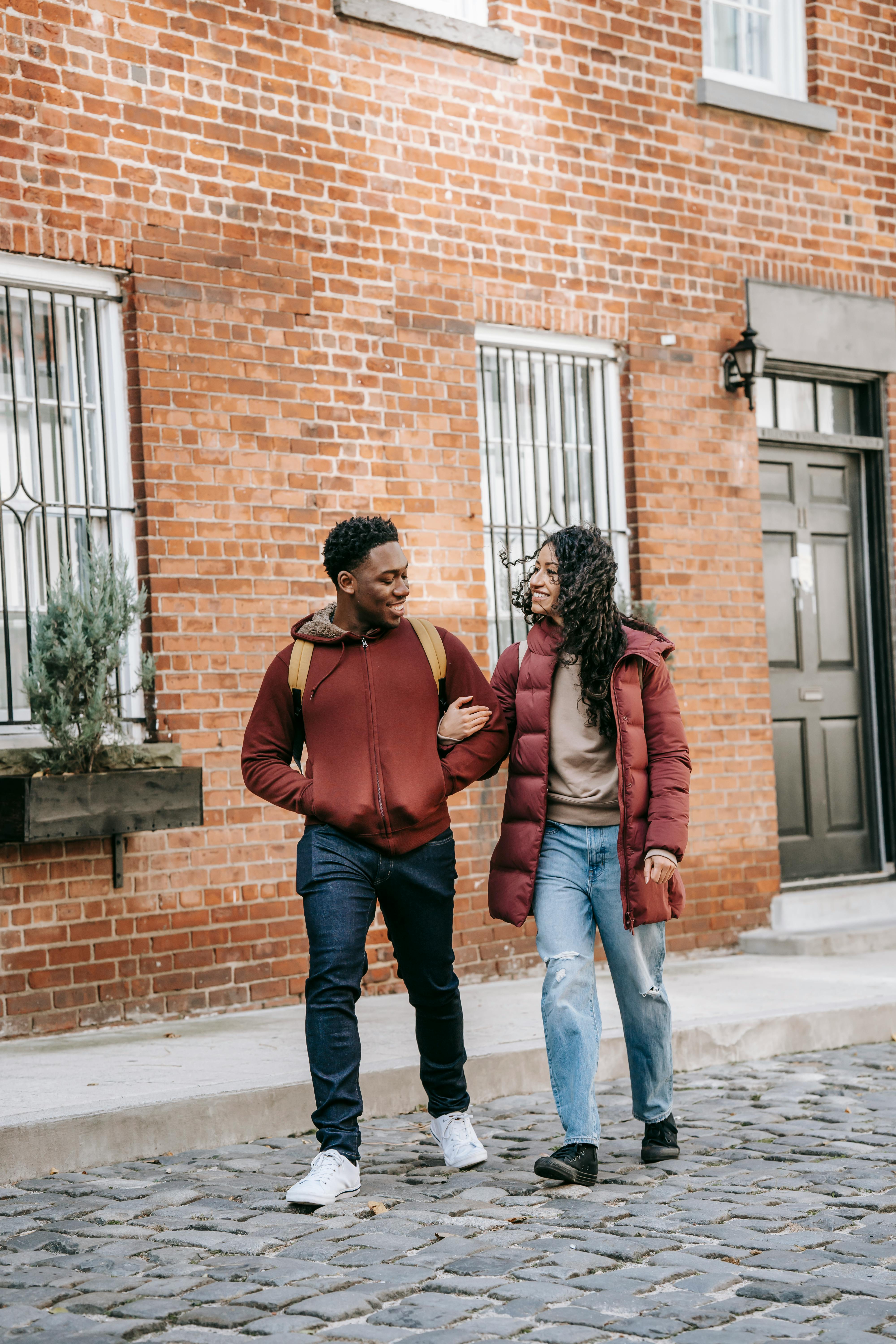 glad multiethnic couple walking on street near brick building