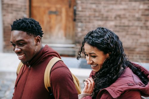Free Cheerful young diverse friends smiling and promenading while speaking on urban street on blurred background of brick building Stock Photo