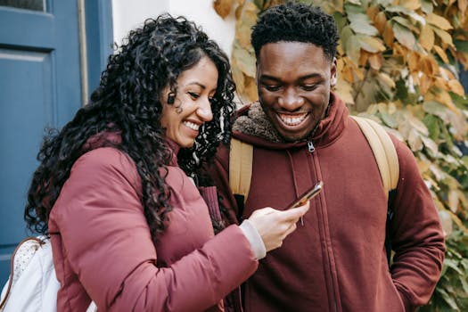 Smiling couple enjoying a moment together while looking at a smartphone outside on a city street.
