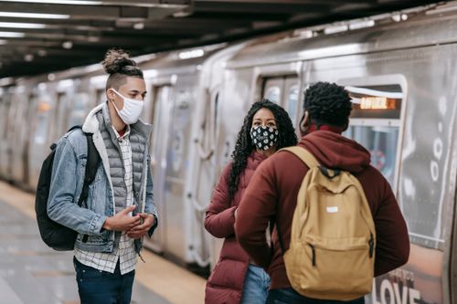 Free Multiracial group of friends with backpacks wearing medical masks chatting while standing in subway station near train on blurred background Stock Photo