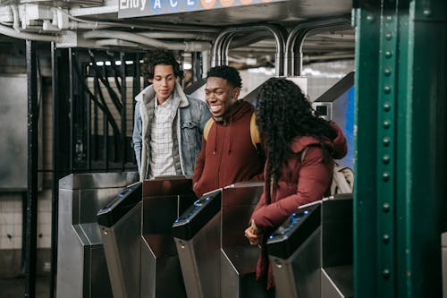 Positive multiethnic group of friends in warm clothes walking through automatic metal gates in subway platform while entering railway station