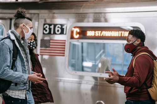 Free Side view of diverse group of friends wearing medical masks looking at each other and having conversation while standing near train on subway station during pandemic Stock Photo