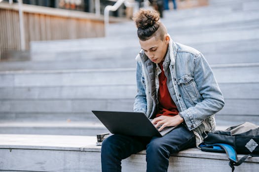 Man with laptop on outdoor steps, focusing on freelance work. Casual style, urban setting.