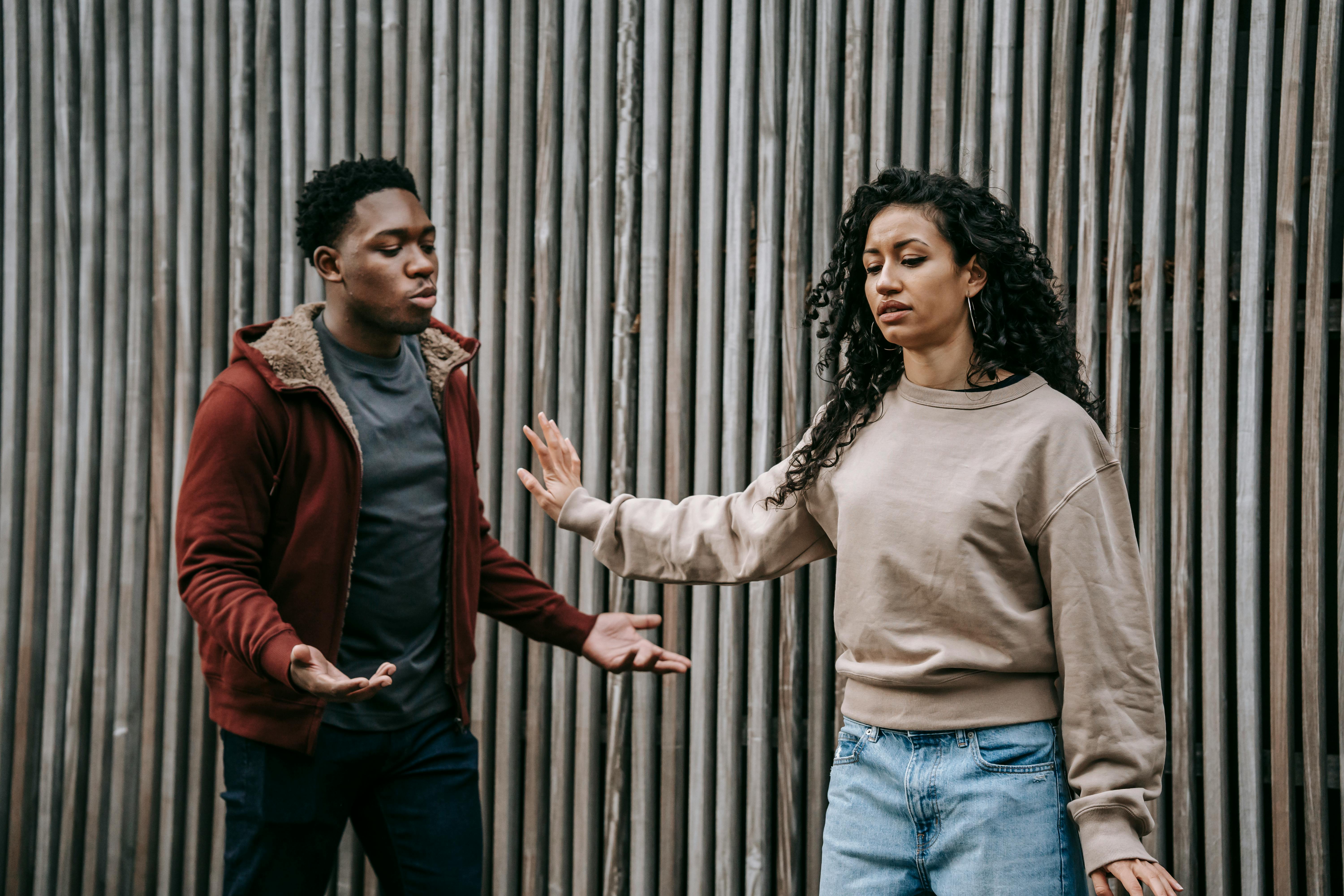 Woman extending her hand in a firm stop gesture toward a man against a corrugated metal wall, demonstrating clear boundary-setting behavior.