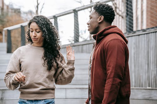 Free Upset ethnic girlfriend with raised hand and concerned African American boyfriend breaking up on street against metal grid on background Stock Photo