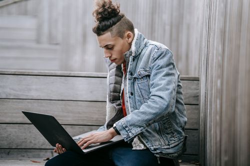 Free Side view of young male with unusual haircut in denim fashionable jacket browsing netbook on street Stock Photo