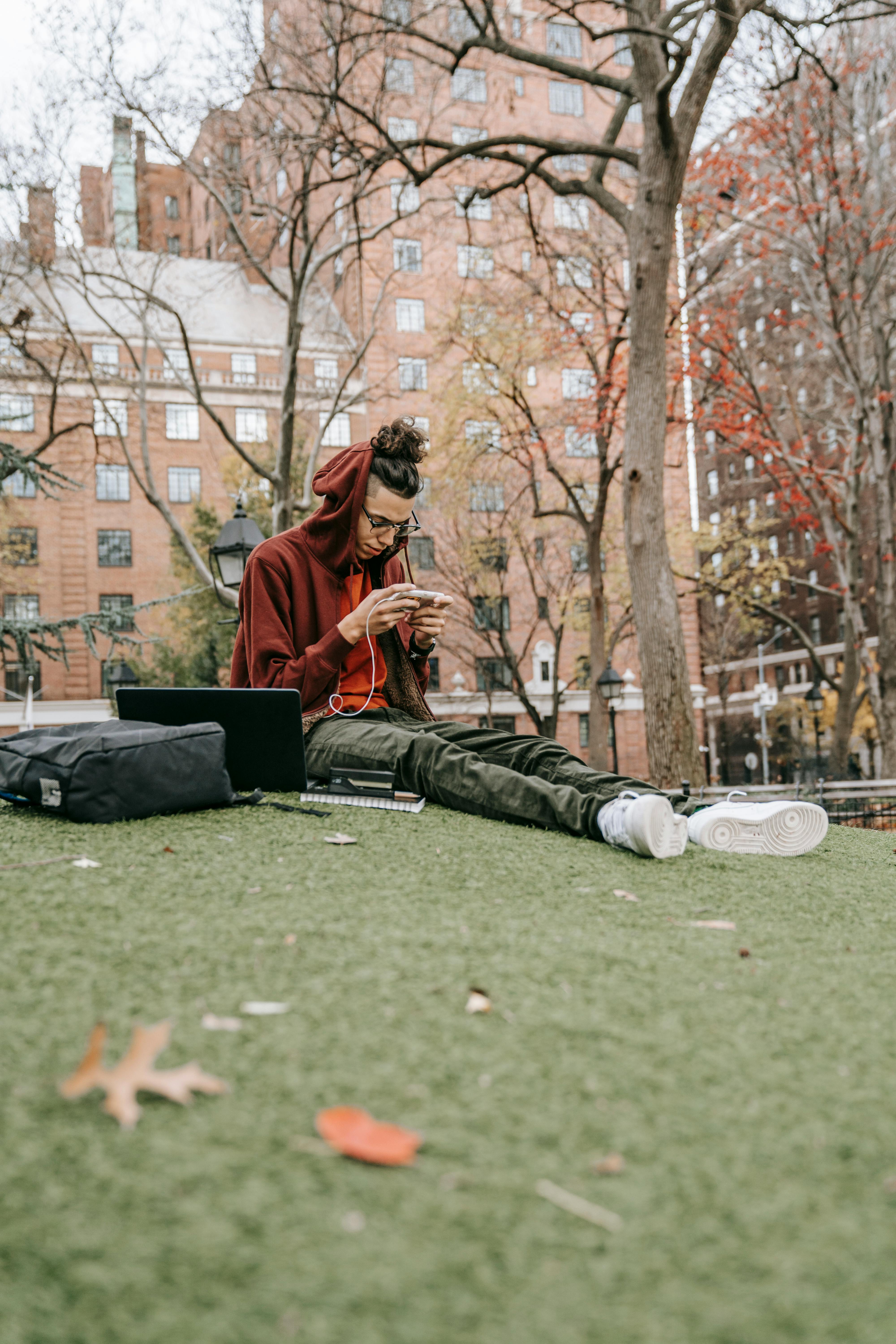 young student using smartphone while doing homework in park