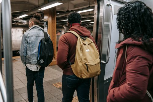 Free Back view of anonymous young multiracial friends in warm clothes and backpacks walking out of train on underground station Stock Photo