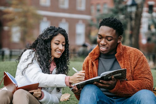 Man and Woman Holding Notebooks While Sitting on Grass