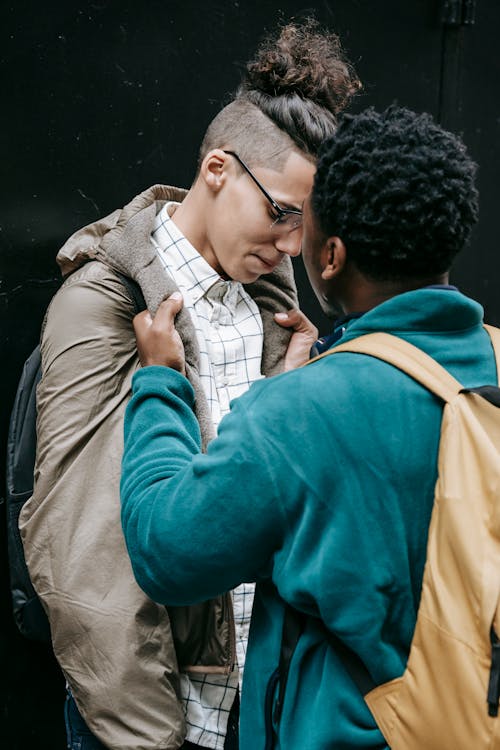 Free Young African American man in casual outfit and bullying classmate while standing in city street with backpack on black background Stock Photo