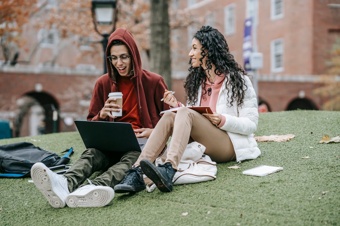 Free Multiethnic friends studying with notepad and netbook on grassy field Stock Photo