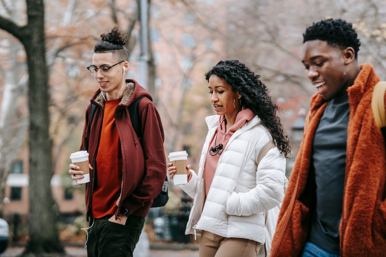confident young multiracial friends in outerwear and backpacks talking