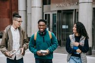Group of smiling multiracial students with books strolling near building