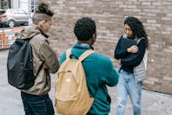 Young multiracial male friends with backpacks offending female with folder on city street near brick wall in daylight