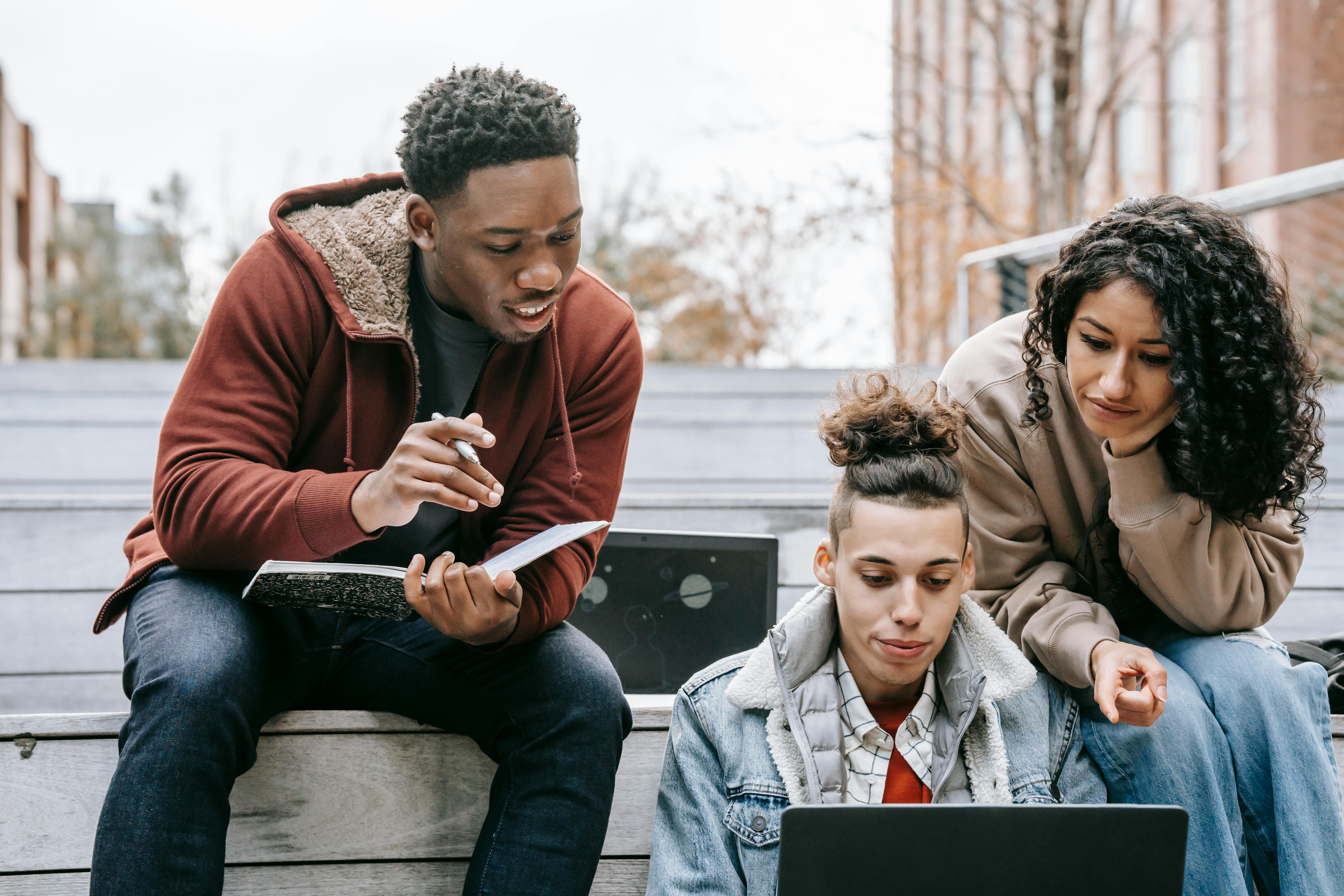 multiracial students studying on netbook with notebook on steps