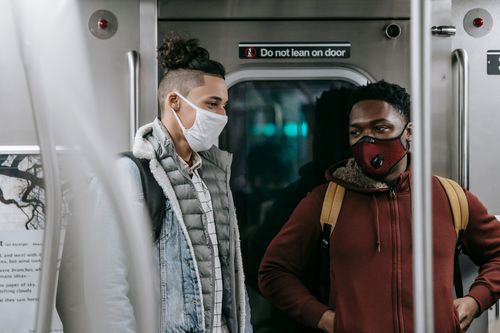 Free Young multiethnic men in protective masks and warm clothes wearing backpacks while standing in light train in metro Stock Photo