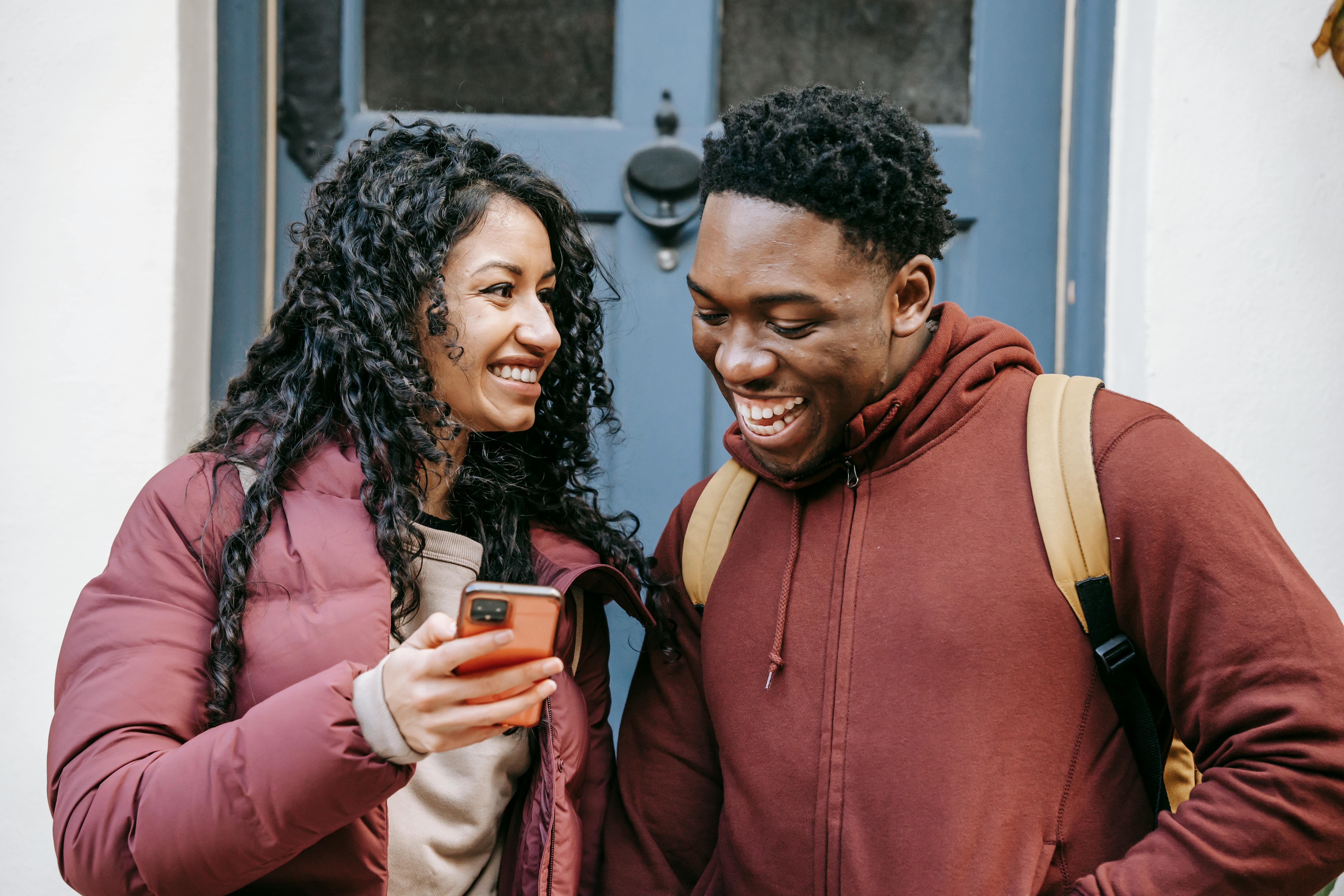 cheerful multiracial couple sharing smartphone on city street