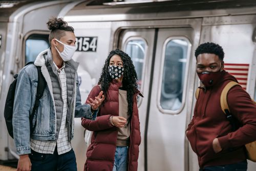 Free Young best multiethnic friends in outerwear and protective masks talking on subway during COVID 19 pandemic Stock Photo