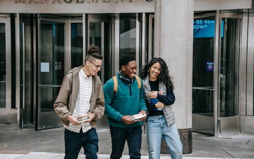 Free Young cheerful multiethnic students with books having fun on urban pavement while speaking in daylight Stock Photo