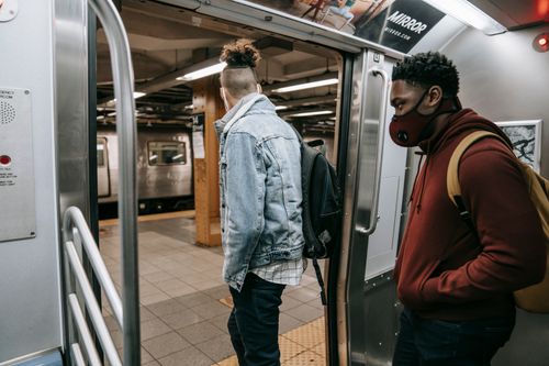 Free Black man in respiratory mask with hand in pocket near unrecognizable partner getting off metro during trip Stock Photo