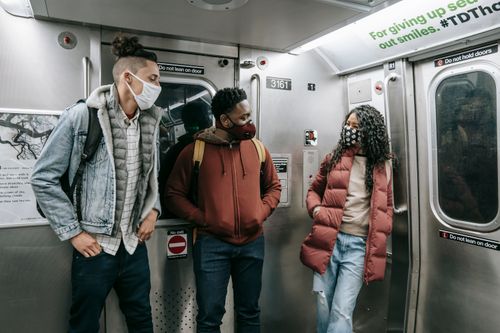 Free Young multiracial friends in masks with hands in pockets talking and looking at each other during journey on metro Stock Photo