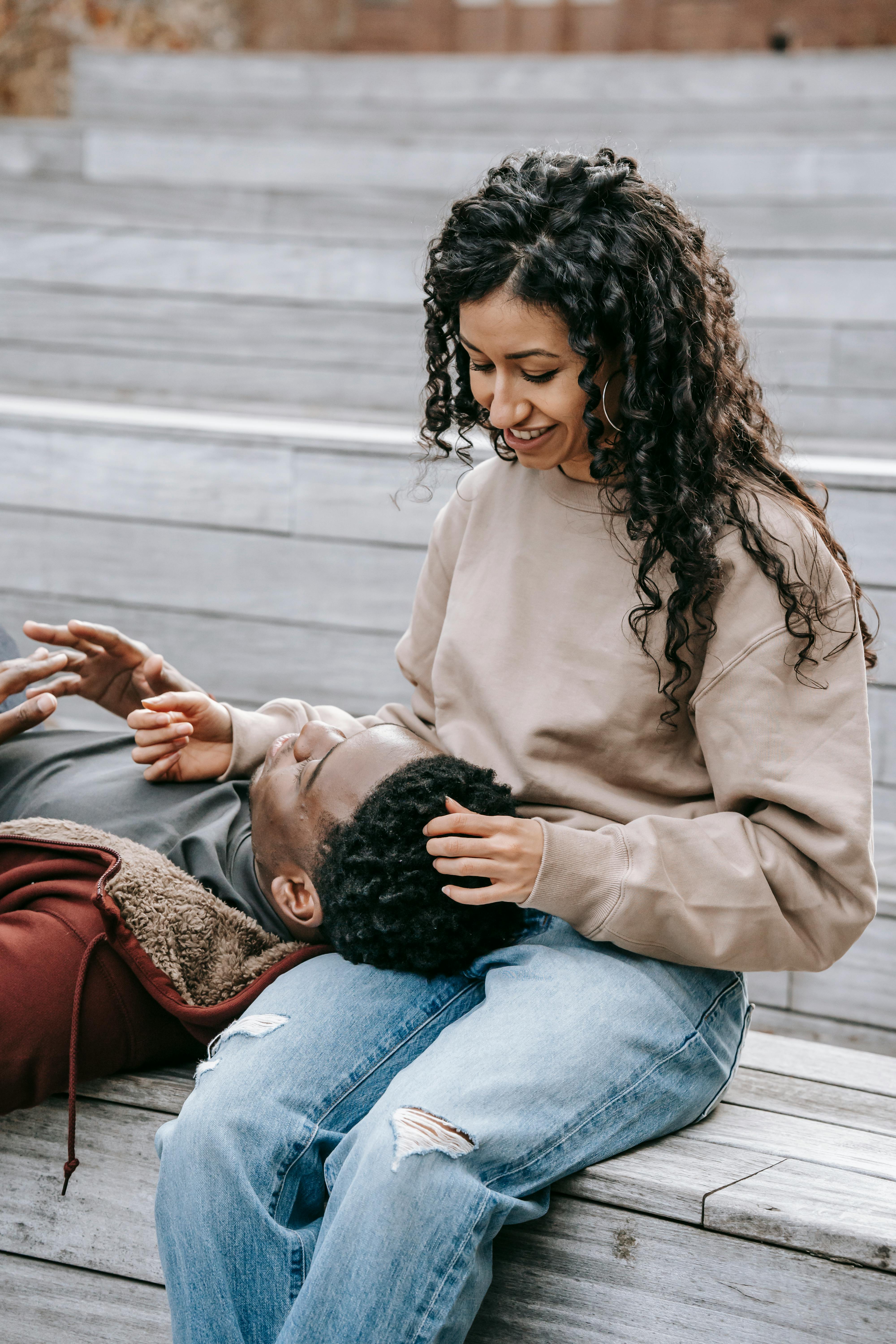 Young smiling ethnic female with curly hair speaking with lying black boyfriend on staircase in daytime