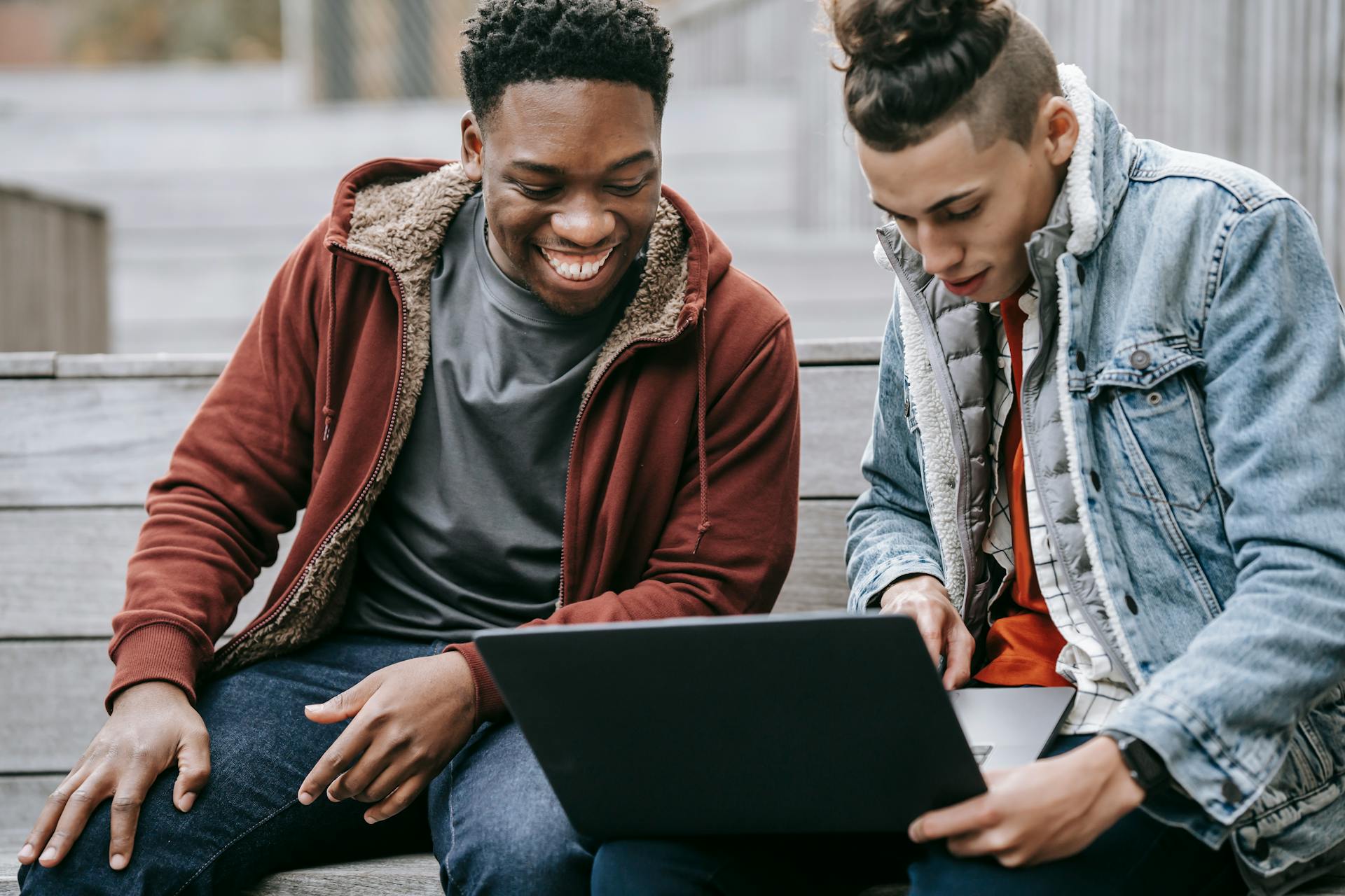 Crop content young multiracial male partners in casual outfit surfing internet on portable computer on urban staircase