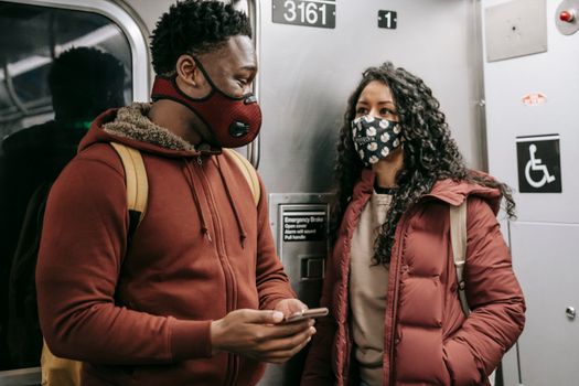 Multiethnic couple in masks with smartphone talking on subway