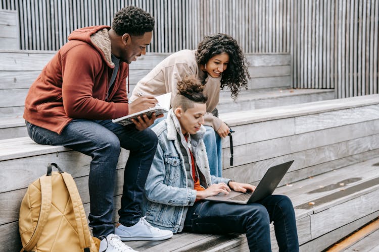 Cheerful Diverse Students Sharing Laptop While Studying On Street Stairs