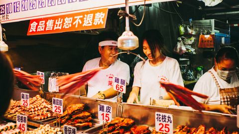 Vibrant scene at a bustling Taiwanese night market food stall with vendors.