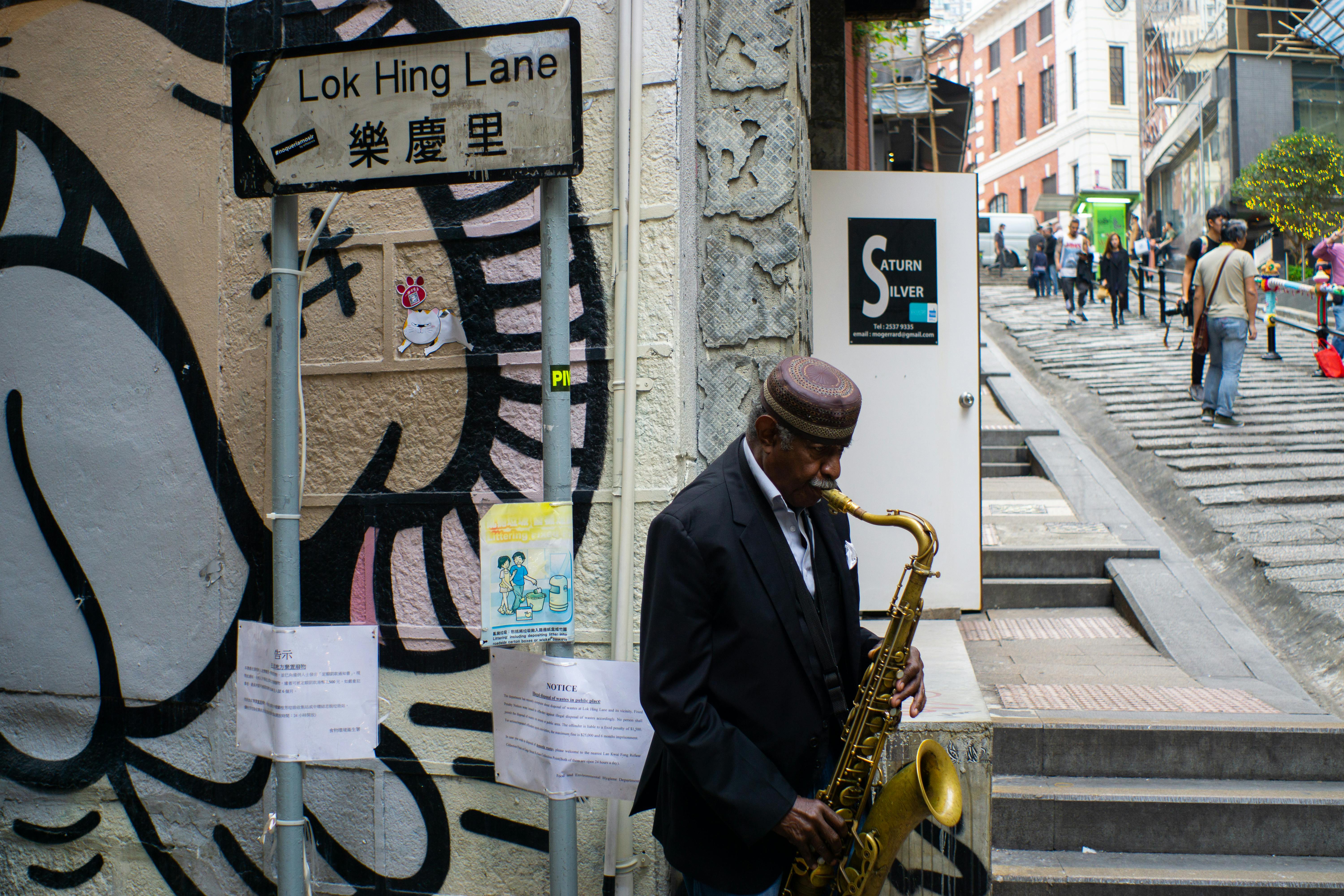 A street musician plays saxophone on Lok Hing Lane, Hong Kong's bustling urban scene.