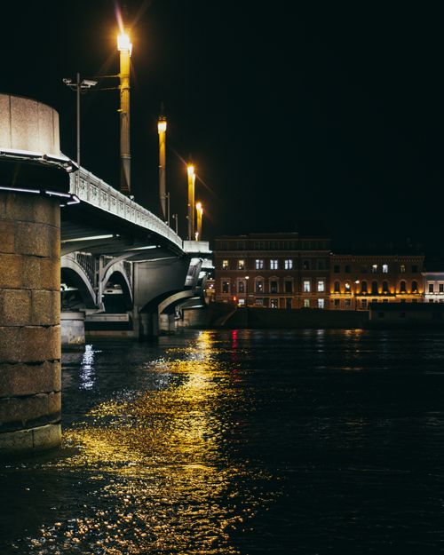 Free Historic arched Kamennoostrovsky Bridge over rippling river flowing near aged buildings against dark night sky in Saint Petersburg Stock Photo