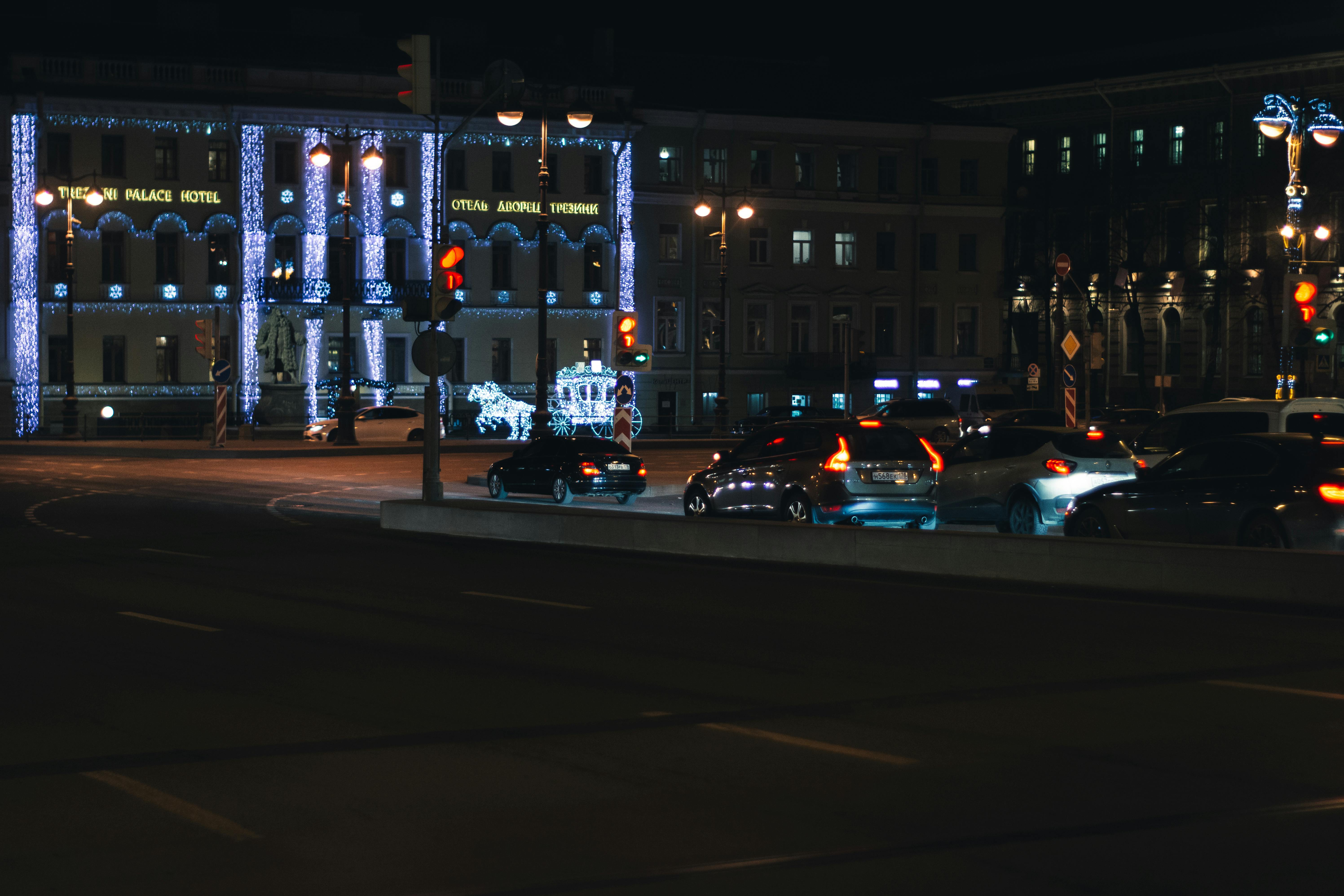 modern cars driving on road near age illuminated buildings in evening