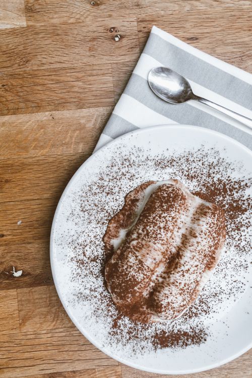 Free Tiramisu sprinkled with cocoa powder on a ceramic plate with spoon and napkin. Stock Photo