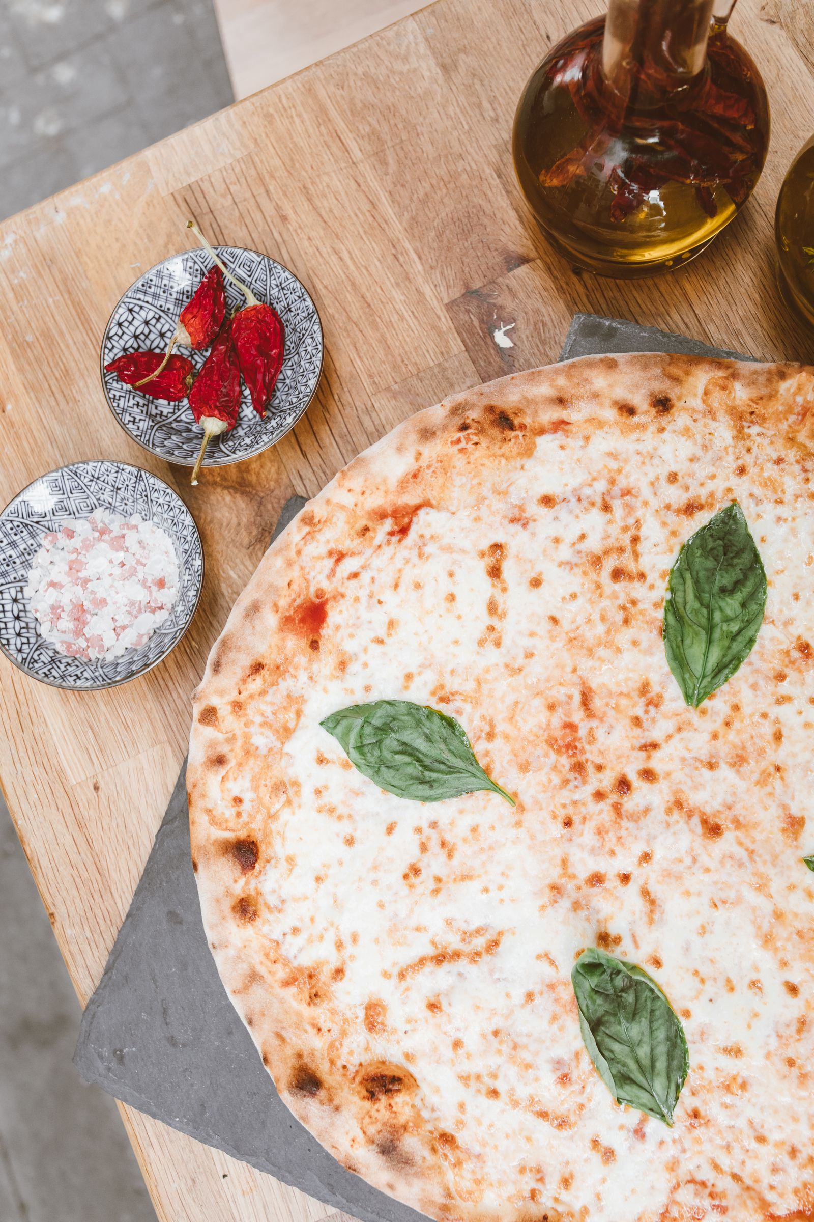 A wood-fired pizza on a rustic table surrounded by fresh ingredients