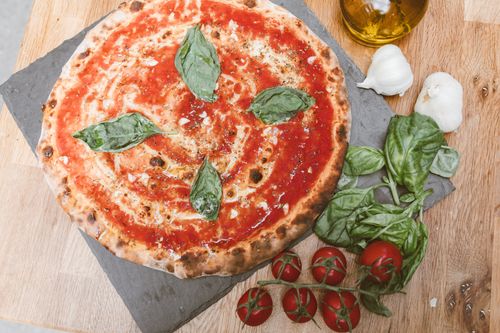 Free Delicious uncooked Margherita pizza with fresh basil, tomatoes, and garlic on a wooden table. Stock Photo