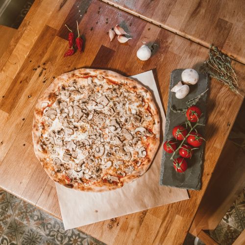 Free Top-down view of a homemade mushroom pizza surrounded by fresh ingredients on a wooden table. Stock Photo