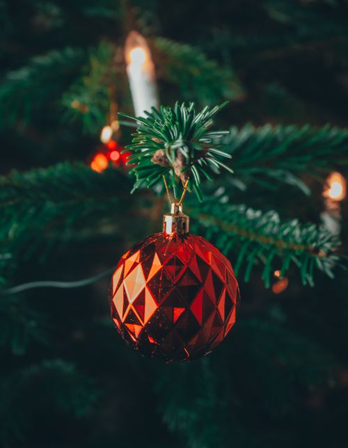 Free A close-up of a red Christmas ball hanging on a decorated tree branch. Stock Photo