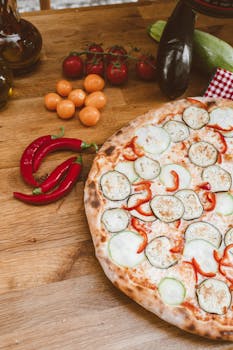 A delicious vegetable pizza with fresh tomatoes, zucchini, and chili peppers on a wooden table.
