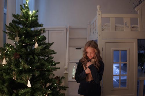 Blonde Girl Embracing Presents by Christmas Tree in Home