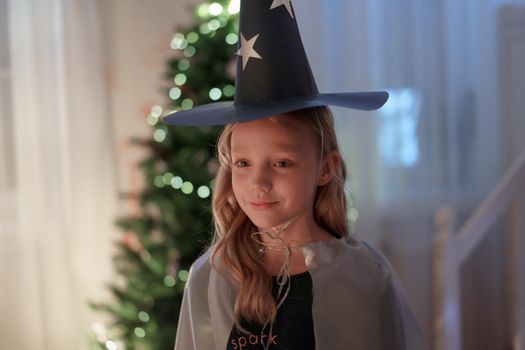 Cute child wearing a wizard costume smiles in front of a Christmas tree indoors.