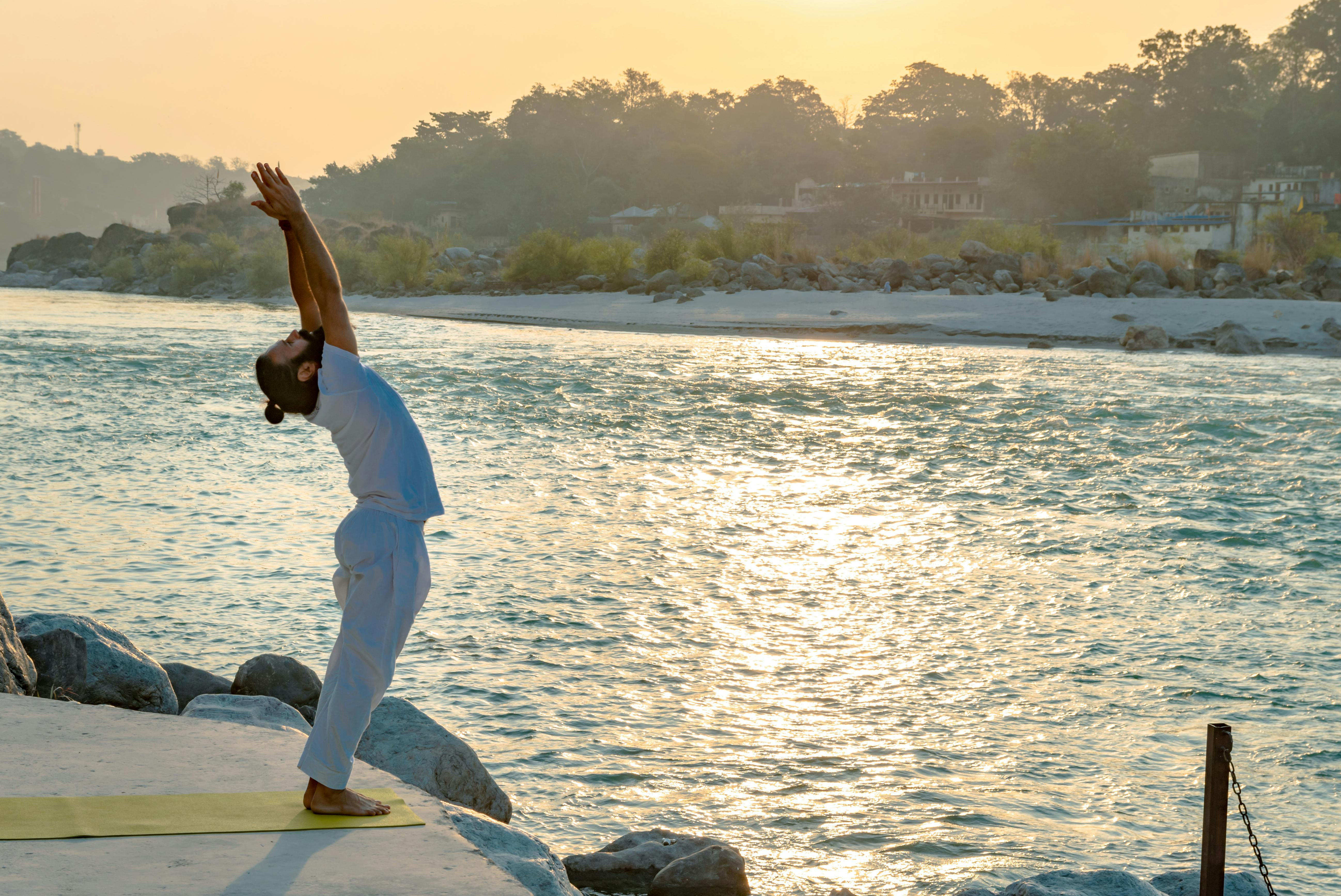 A man performs yoga by the Ganges River in Rishikesh at sunrise, embracing tranquility and mindfulness.
