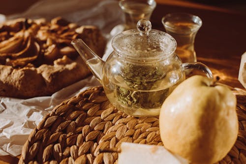 A Teapot Beside Pear on a Woven Plate