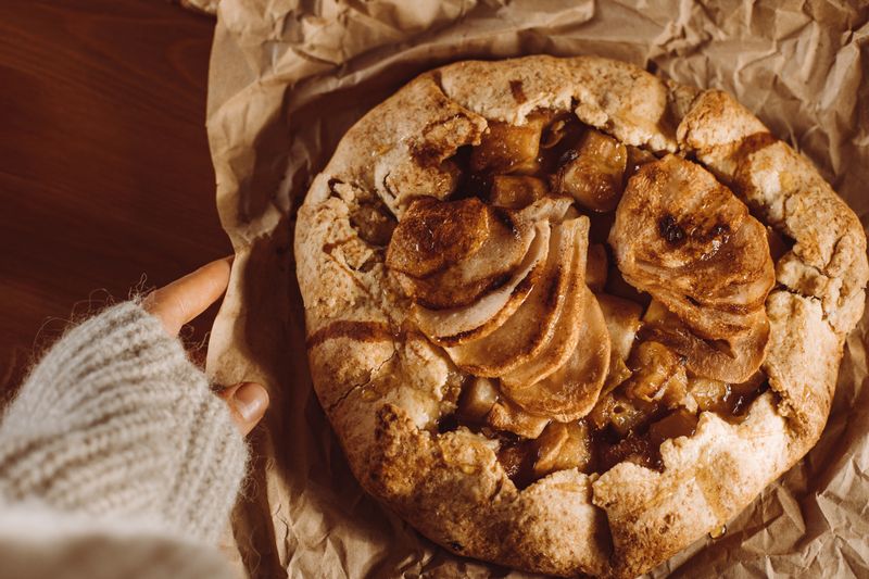 A top-down view of a homemade apple galette on brown paper with a cozy sweater in sight.