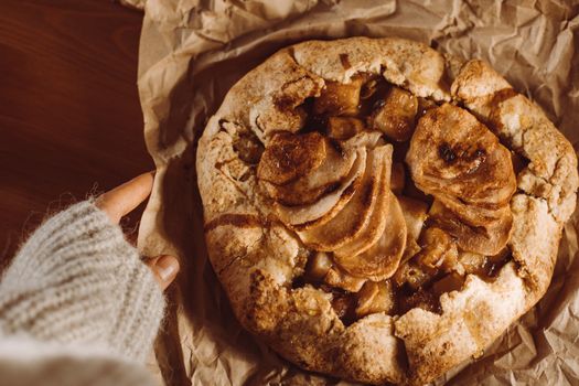 A top-down view of a homemade apple galette on brown paper with a cozy sweater in sight.