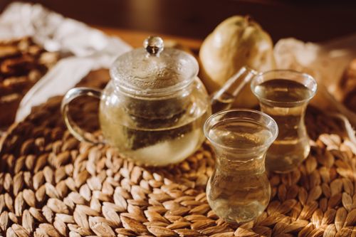 Free Glass teapot with tea and two glasses beside a ripe pear on woven mat, warm afternoon vibe. Stock Photo