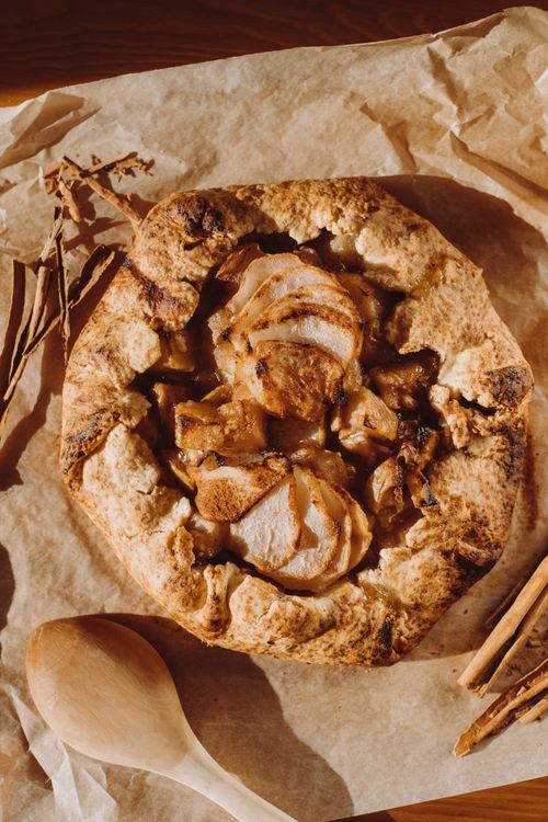Free Warm apple galette on parchment, surrounded by cinnamon sticks, perfect for dessert lovers. Stock Photo
