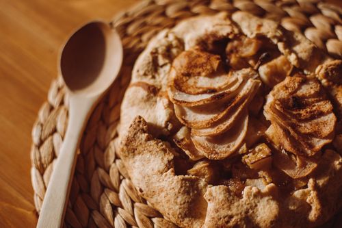 Free Top view of a freshly baked apple galette on a woven placemat with a wooden spoon beside it. Stock Photo