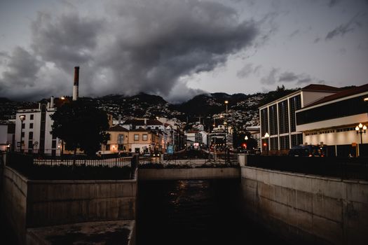 Dramatic evening view of Funchal, Madeira with a cloudy sky and city lights illuminating the streets.