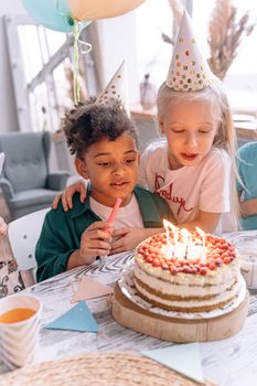 Two children enjoy a birthday celebration with a cake and party hats.
